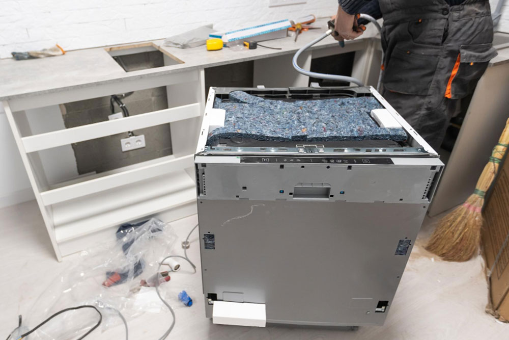 Installation eines unverkleideten Geschirrspülers in einer Küche, die gerade eingerichtet wird.