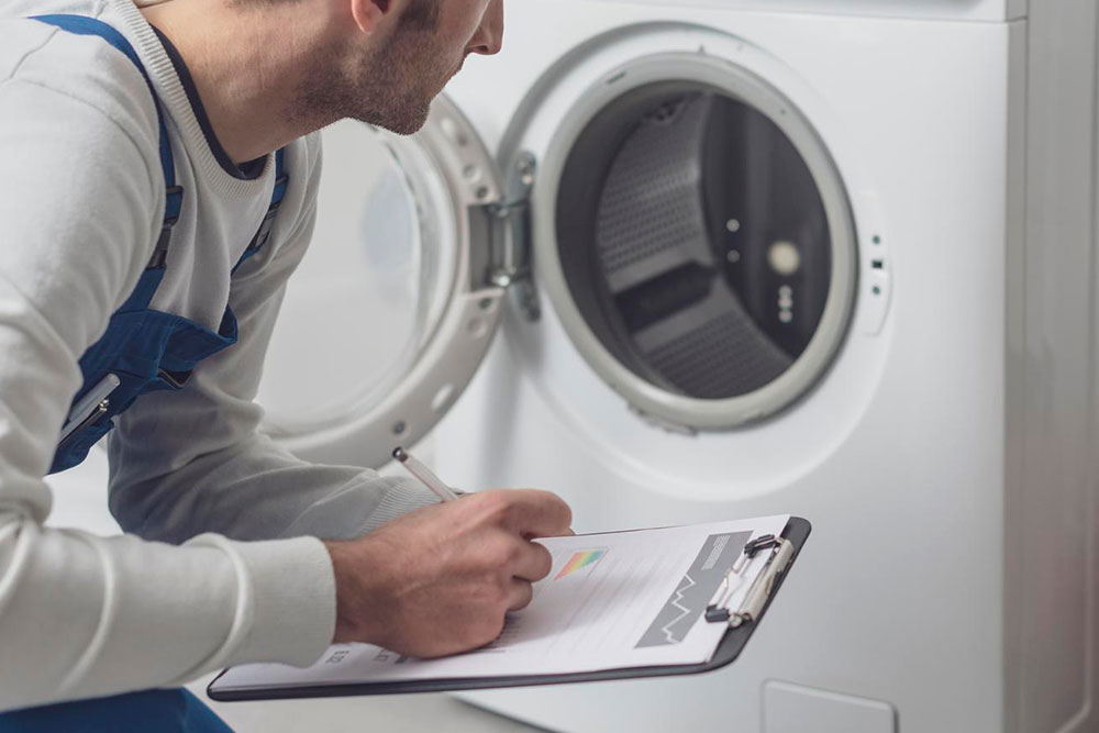 Techniker füllt ein Dokument auf einem Klemmbrett vor einer geöffneten Waschmaschine aus.