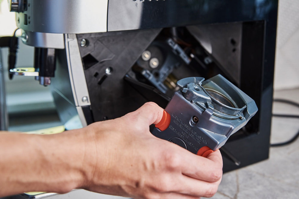 Eine Hand, die ein Teil einer Kaffeemaschine vor einer Kaffeemaschine hält.